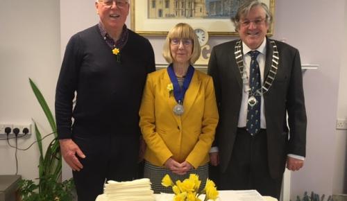 L-R Gareth Phillips from Corton House Board of Trustees, Deputy Lord Mayor of Norwich Councillor Caroline Ackroyd, and President of Norwich Welsh Society David Charles. They are smiling and standing in front of a table of daffodils and Welsh cakes ready t