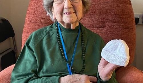 Corton House care home resident Elsie smiles while holding baby hats knitted for the local hospital in Norwich